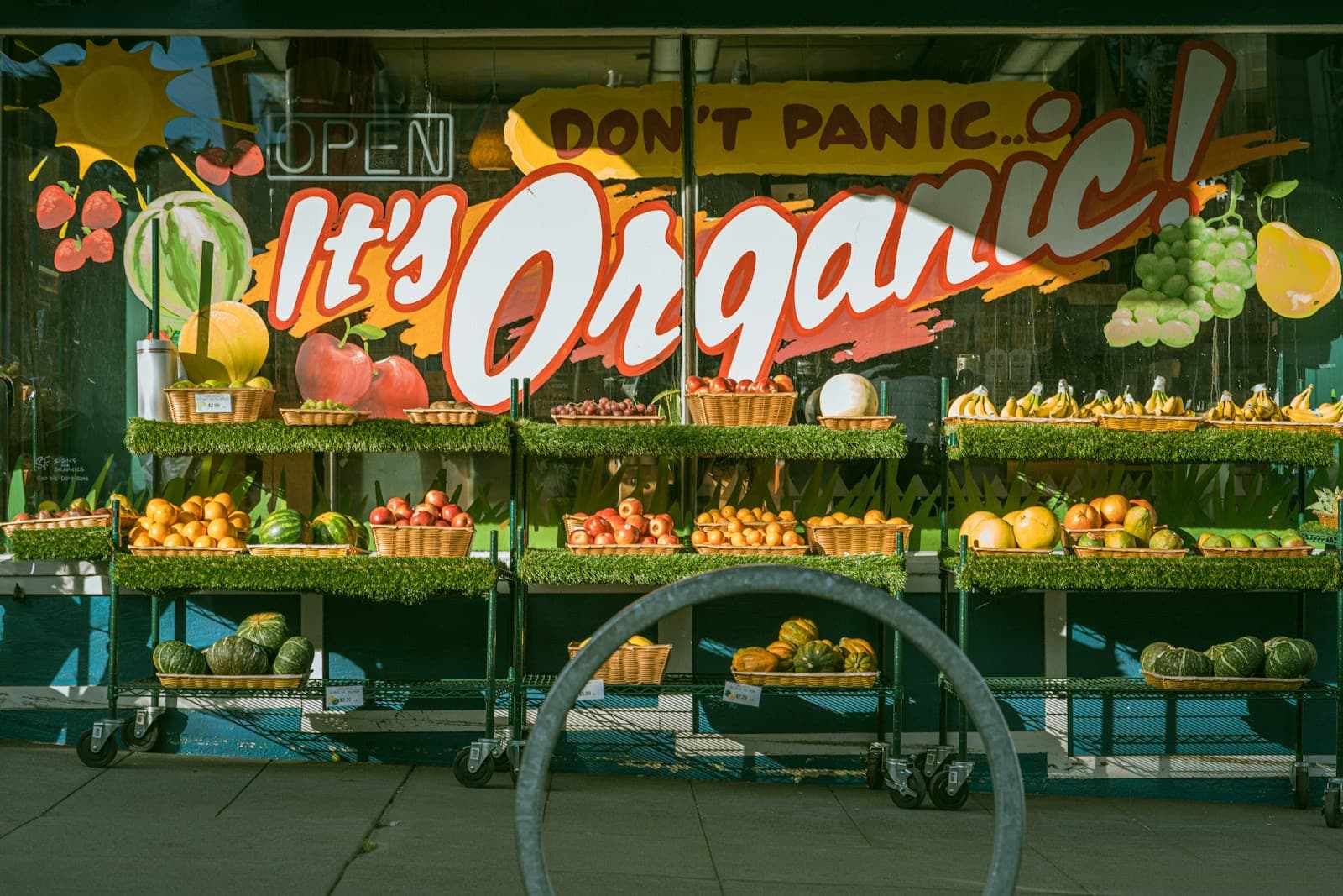 A grocery storefront window with baskets of fruit and squash on tiered display shelves.